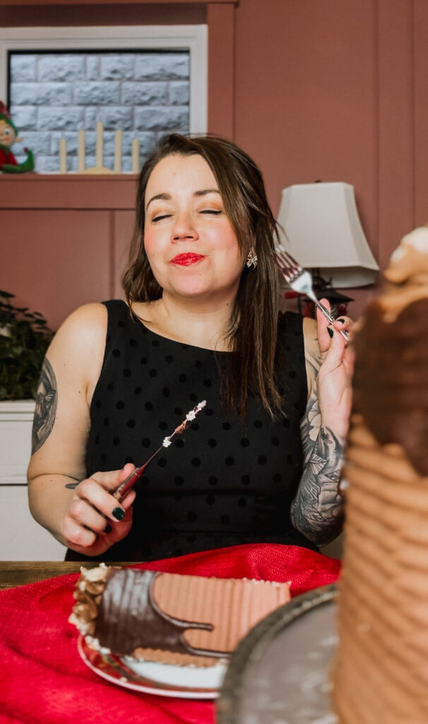 Woman enjoying a slice of chocolate cheesecake at a festive holiday table, holding a fork and smiling during a dessert taste test.