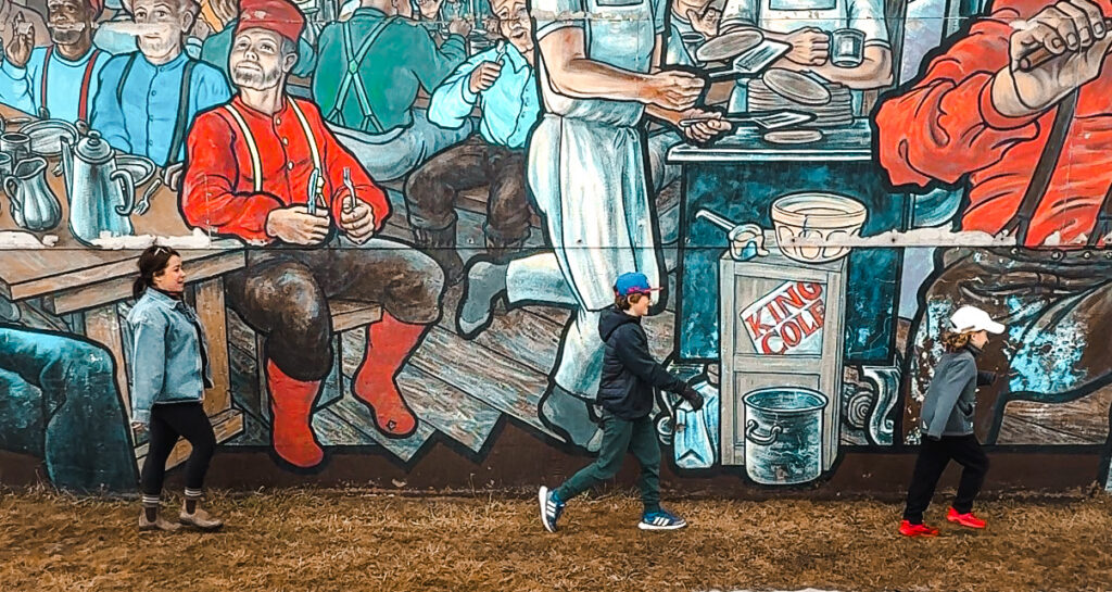 Woman and two children walking in front of the King Cole Tea mural in Sussex, New Brunswick