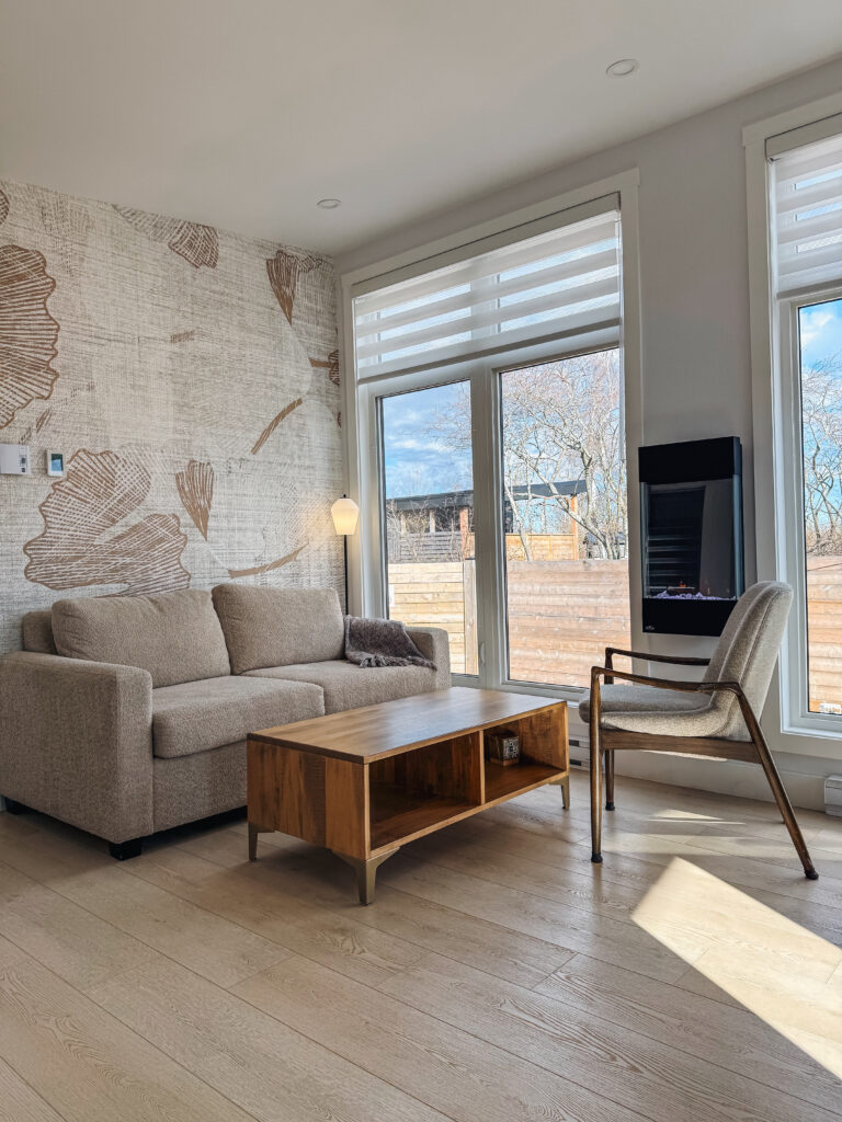 Bright modern living room inside a Glamping Aboiteau unit with a large botanical wallpaper feature wall electric fireplace and mid-century lounge chair