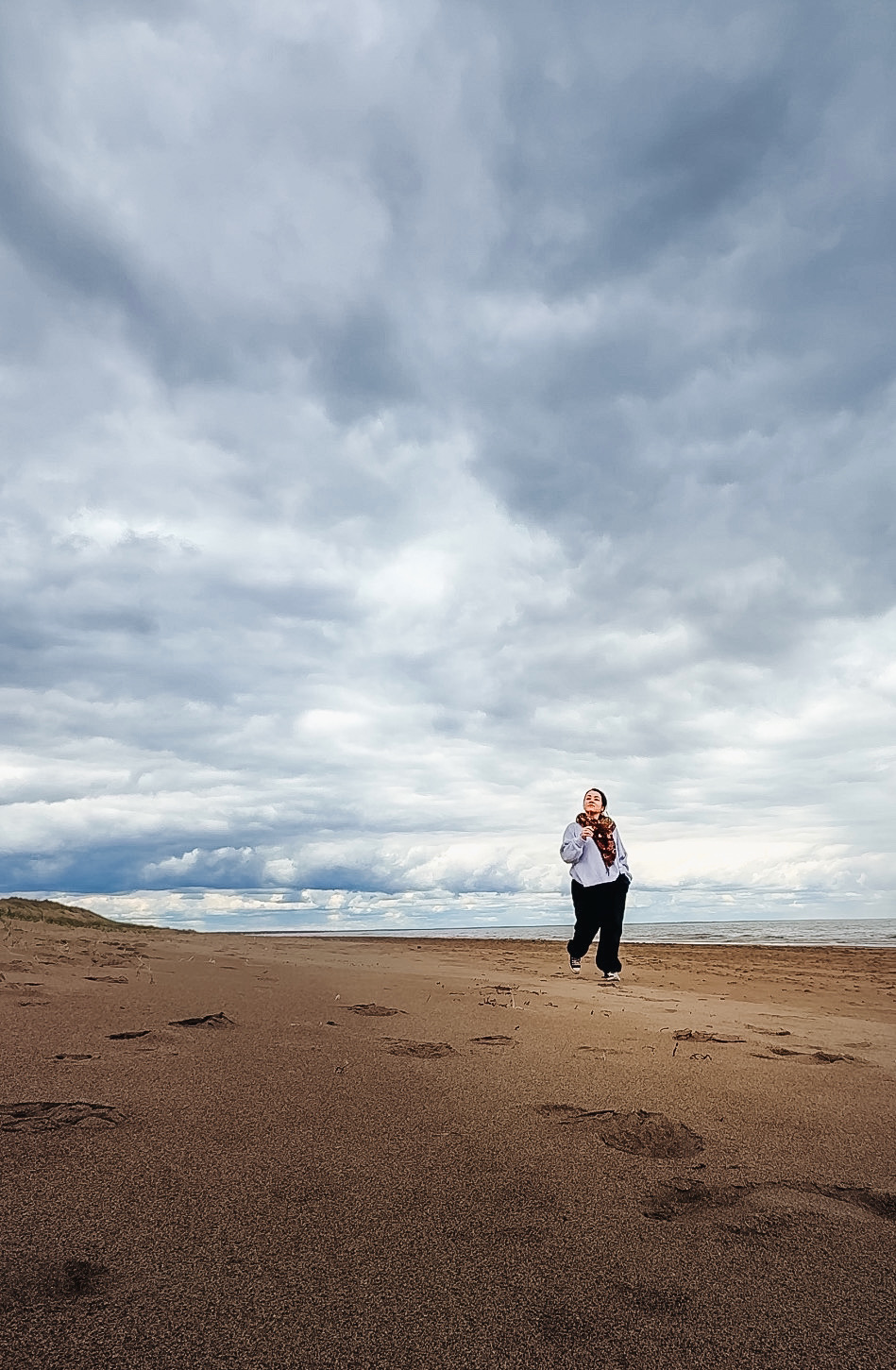 Woman walking alone on Aboiteau Beach in Cap-Pelé New Brunswick under a wide dramatic cloudy sky
