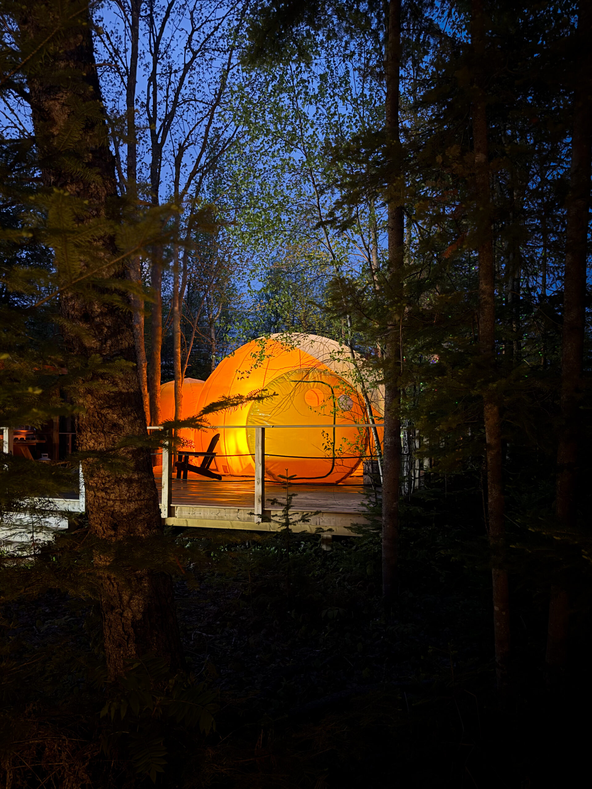 Estrella Glamping bubble glowing amber among the trees at dusk on the Acadian Peninsula
