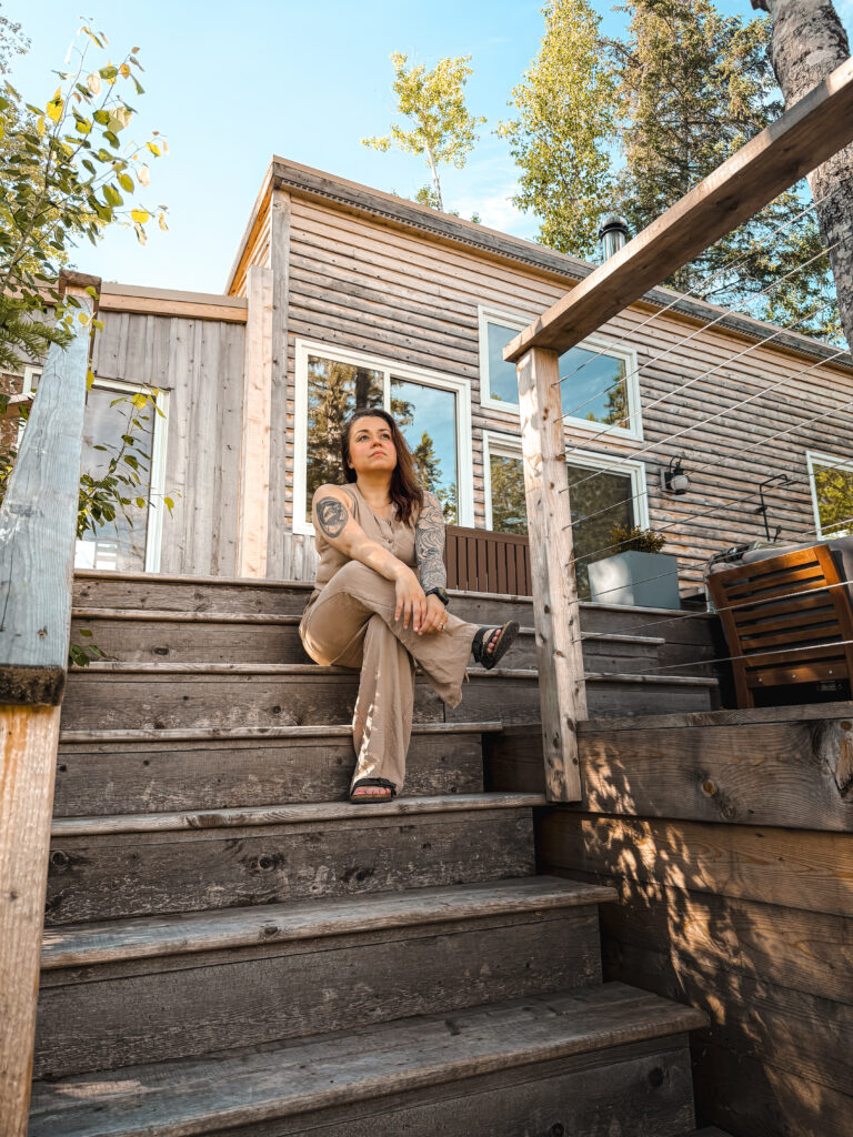 Melissa Danielle sitting on the wooden cabin steps at Eagles Nest, looking upward and surrounded by trees