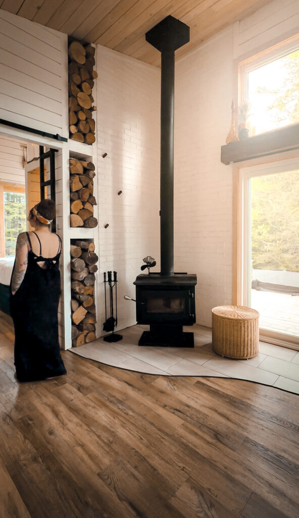 nterior of Eagles Nest cabin showing a black wood stove with stacked firewood built into the white shiplap wall
