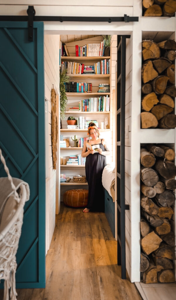 Melissa Danielle reading in the Eagles Nest library nook, framed by a teal barn door and floor-to-ceiling bookshelves